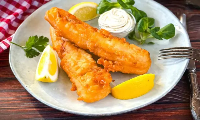 Zwei goldbraun frittierter Fisch mit Zitronenspalten, Sauce und Salat auf einem Teller.