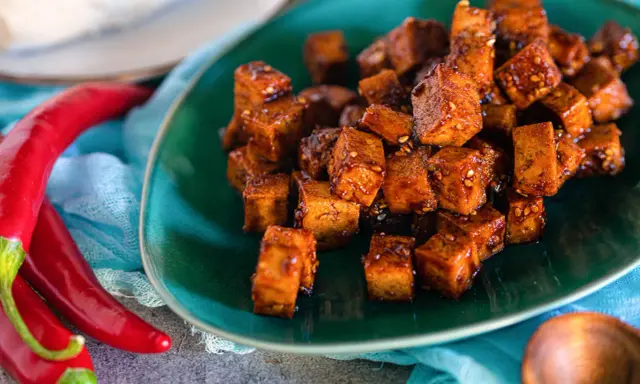 Würzig gebratene Tofuwürfel auf einem grünen Teller, daneben rote Chilis. So schmeckt Tofu!