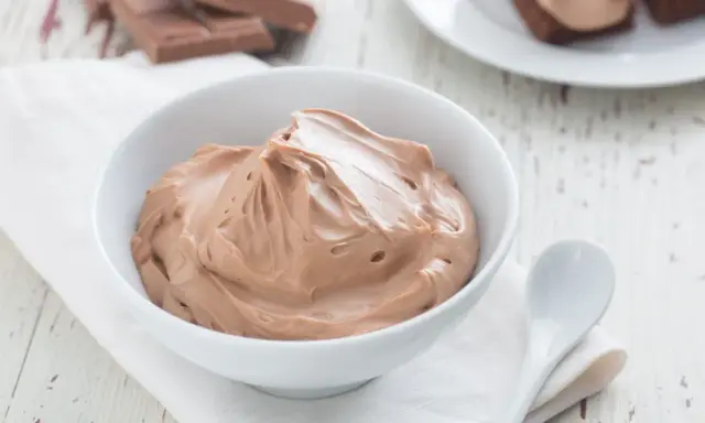 Cremige Schokoladen-Namelaka in einer Schüssel, daneben ein Löffel und Schokoladenstücke.