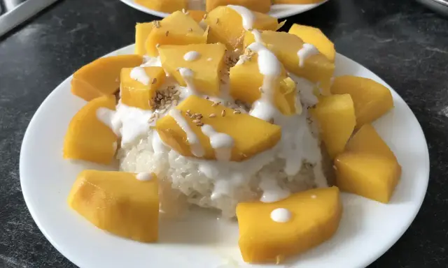 Ein Teller mit Klebreis, garniert mit saftigen Mango-Stücken, Kokosmilch und Sesam. Ein köstlicher **thai dessert mango**.