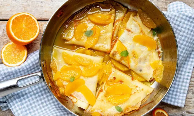 Crêpes Suzette im Originalrezept: zarte Pfannkuchen in Orangensauce mit frischen Orangenspalten und Minze garniert.