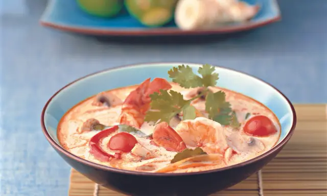 Eine cremige garnelensuppe asiatisch mit Garnelen, Pilzen und Tomaten, garniert mit Koriander.