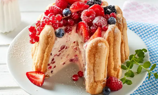 Eine köstliche Charlotte Torte, umhüllt von Löffelbiskuits und üppig belegt mit frischen Beeren wie Erdbeeren, Himbeeren und Johannisbeeren.