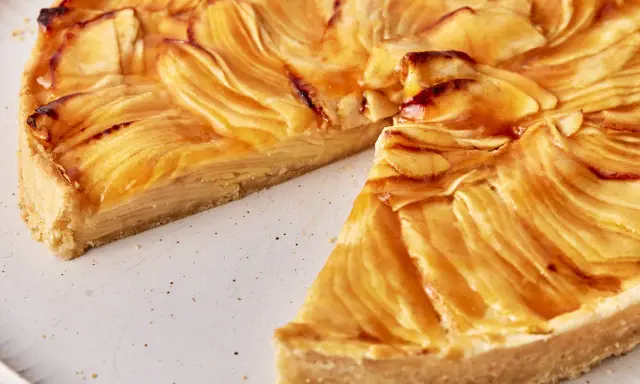 Eine köstliche Tarte au Pomme mit karamellisierten Apfelscheiben auf einem knusprigen Boden, auf einem rustikalen Teller.