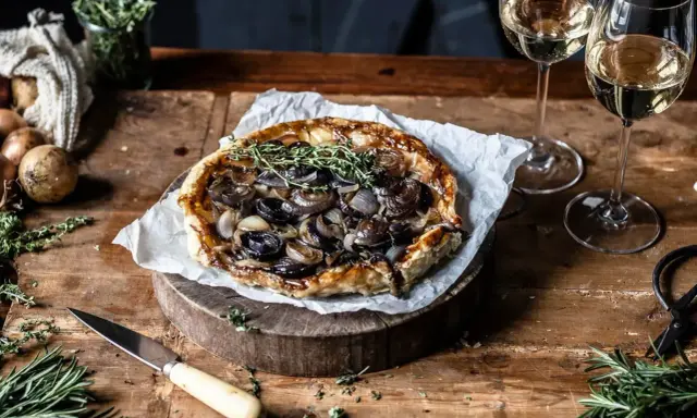 Herzhafte Tarte Tatin mit karamellisierten Zwiebeln und frischen Kräutern, serviert mit Weißwein.