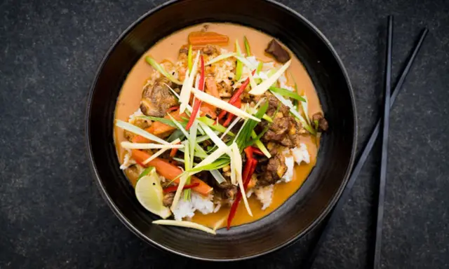 Ein aromatischer Thai Curry Rind mit Reis, Karotten und frischen Kräutern, garniert mit Limette.