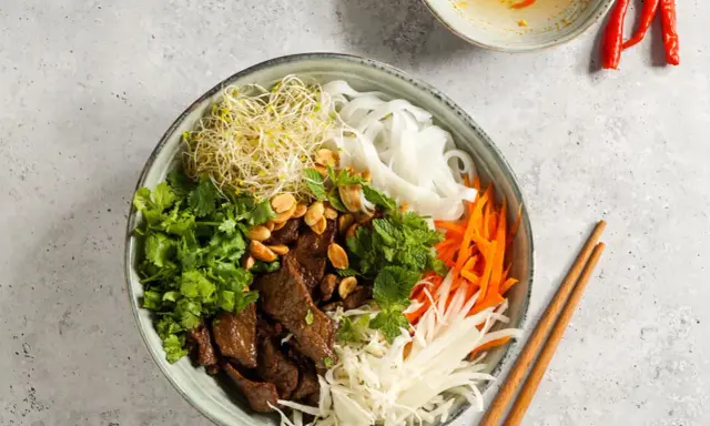 Bun bo nam bo: Reisnudeln, Rindfleisch, Sprossen, Karotten, Kohl und Kräuter in einer Schüssel, garniert mit Erdnüssen.