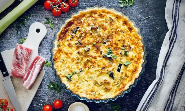 Herzhafte Quiche mit Speck und Lauch, perfekt für herzhafte Quiche Rezepte. Dazu frische Tomaten und Kräuter.