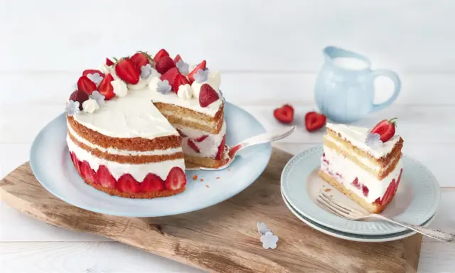 Eine köstliche Erdbeer Basilikum Torte mit frischen Erdbeeren und Sahne, ein Stück davon auf einem Teller.