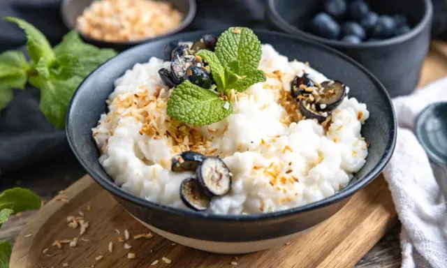 Cremiger Milchreis mit Wasser gekocht, garniert mit Blaubeeren, Minze und gerösteten Kokosflocken. Ein Genuss, der an Kindheit erinnert.