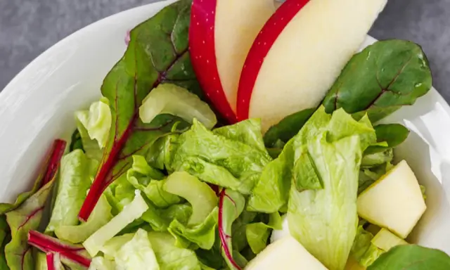 Frischer Romana Salat mit Apfelstücken und roten Mangoldblättern in einer weißen Schüssel.
