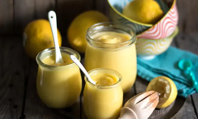 Leichte Zitronencreme im Thermomix zubereitet, serviert in Gläsern mit Löffeln, daneben frische Zitronen und ein Zitruspresse.