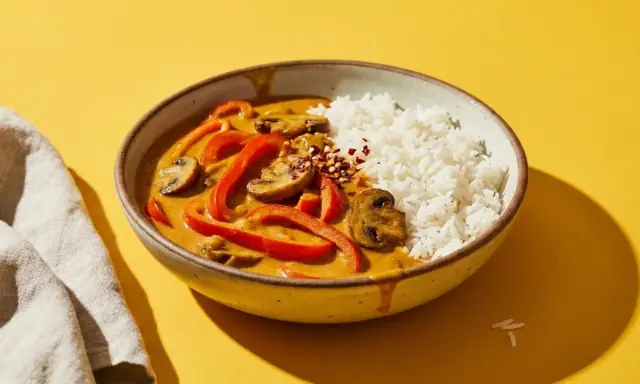 Schüssel mit Reis und rotem Curry, das mit Paprika und Pilzen verfeinert ist. Ein Hauch von Chiliflocken deutet an, dass dieses rote Curry scharf ist.