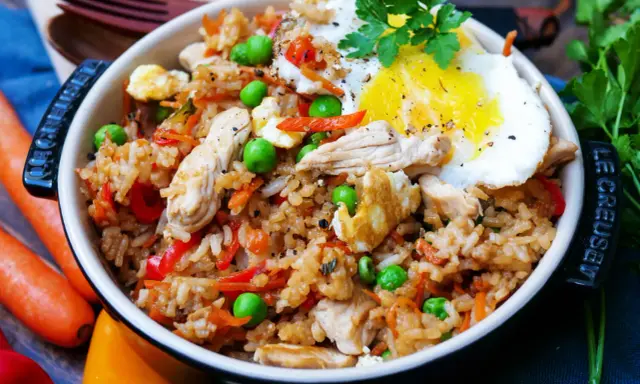 Ein köstliches Nasi Goreng Rezept original: Reis mit Hühnchen, Erbsen, Karotten, Paprika und Spiegelei, garniert mit Petersilie.