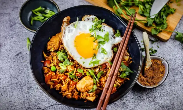 Was ist Nasi Goreng? Ein Teller mit gebratenem Reis, Hühnchen, Erbsen und einem Spiegelei, garniert mit Koriander und Frühlingszwiebeln.