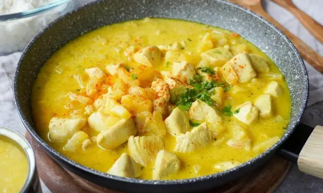 Ein köstlicher Curry mit Ananas und Hähnchenstücken in einer cremigen gelben Sauce, garniert mit Petersilie und Paprikapulver.