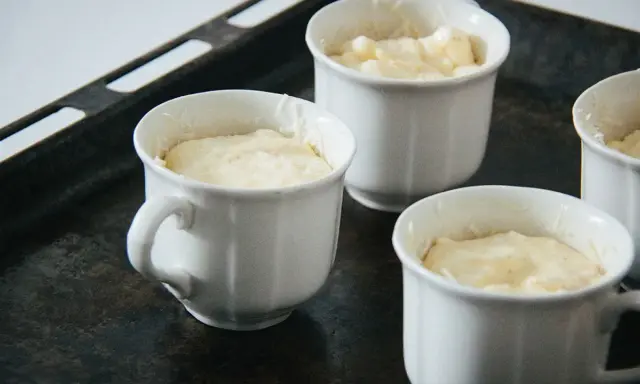 Vier weiße Förmchen mit luftiger Masse für ein Käsesoufflé stehen auf einem Backblech.
