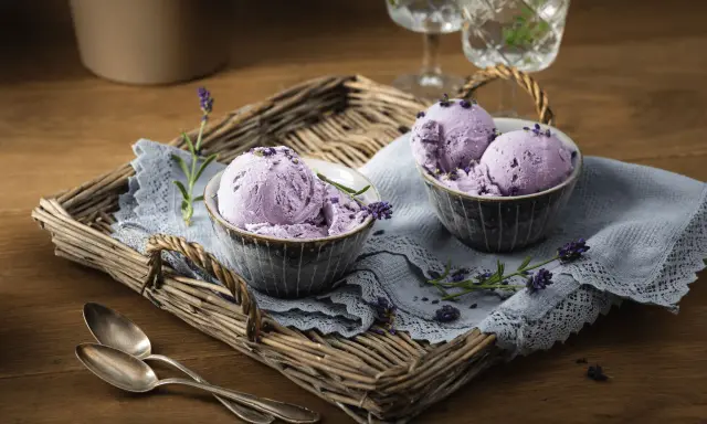 Zwei Schalen mit cremigem Lavendeleis, garniert mit Lavendelblüten, auf einem rustikalen Tablett.