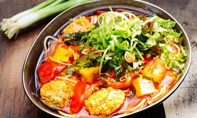 Herzhaftes Bun Rieu mit Tofu, Tomaten und frischen Kräutern, garniert mit Frühlingszwiebeln.