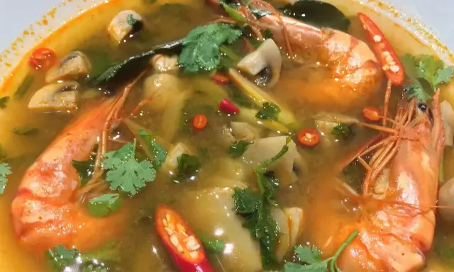 Eine dampfende Schüssel mit scharfer Thai Suppe, gefüllt mit Garnelen, Pilzen und Chili.