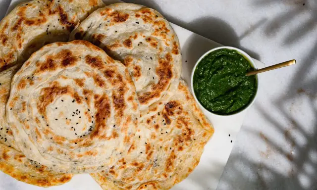 Fluffiger Roti Canai mit schwarzen Sesamkörnchen, daneben eine Schale mit grüner Chutney-Sauce.