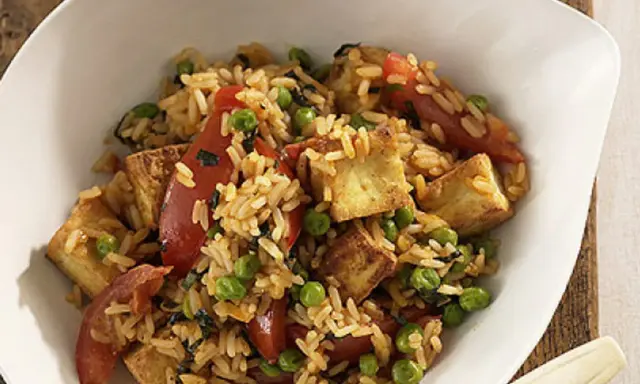 Herzhafter pilaw reis mit gebratenem Tofu, Erbsen und Tomatenstücken in einer weißen Schüssel.