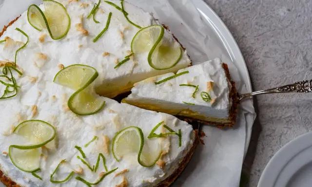 Eine köstliche Limetten Tarte mit luftiger Baiserhaube, garniert mit frischen Limettenscheiben und Zesten. Ein Stück wird gerade serviert.