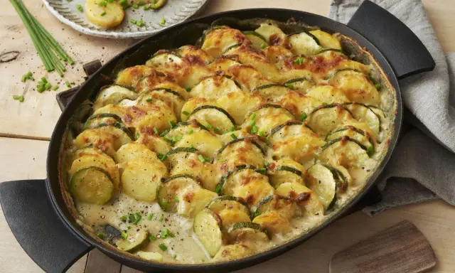 Herzhafte zucchini kartoffel rezepte: überbackene Scheiben aus Zucchini und Kartoffeln in cremiger Sauce, garniert mit Schnittlauch.