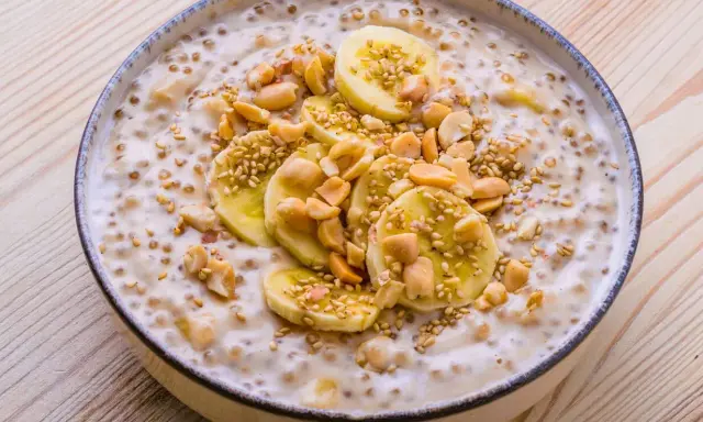 Schüssel mit cremigem vietnamesischem Dessert, garniert mit Bananenscheiben, Erdnüssen und Sesam.