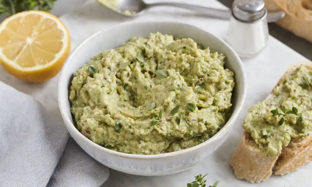 Ein cremiger Zucchini-Aufstrich mit Kräutern und Zitrone, serviert auf Brot.