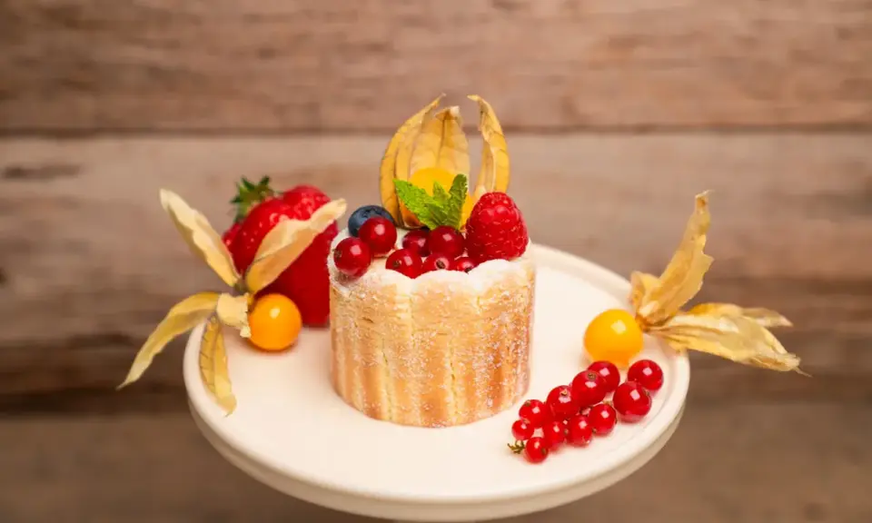 Ein kleiner Charlotte Kuchen, verziert mit frischen Beeren, Physalis und einem Hauch Puderzucker.