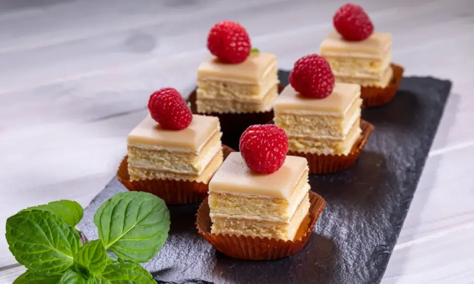 Sechs moderne Petit Fours mit Himbeeren und Minze auf einem Schieferbrett.