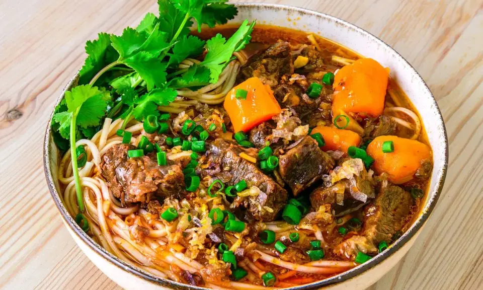 Herzhaftes Bo Kho mit zarten Rindfleischstücken, Karotten und Nudeln, garniert mit Koriander und Frühlingszwiebeln.