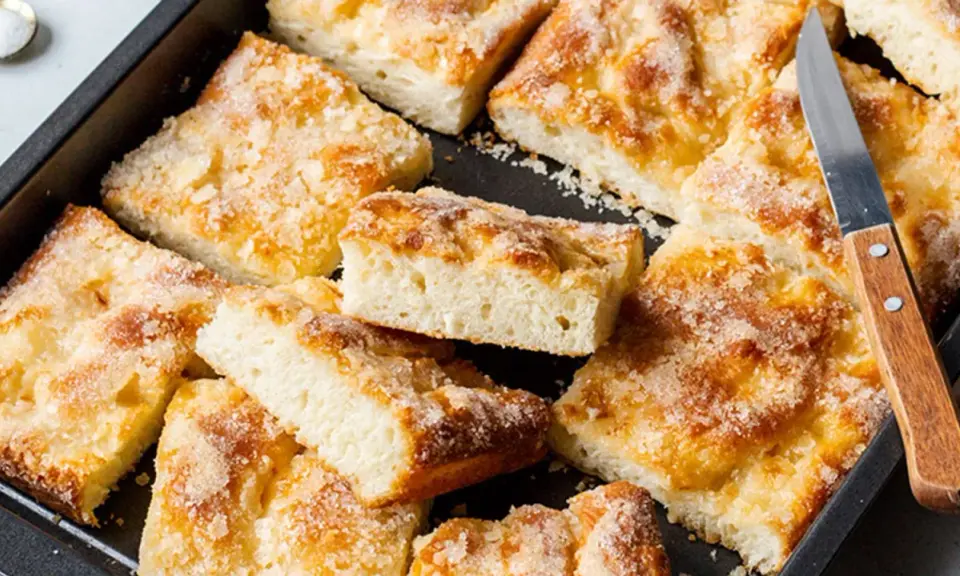 Ein Blech mit saftigem, **schneller Butter zuckerkuchen**, in Stücke geschnitten. Ein Messer liegt bereit.