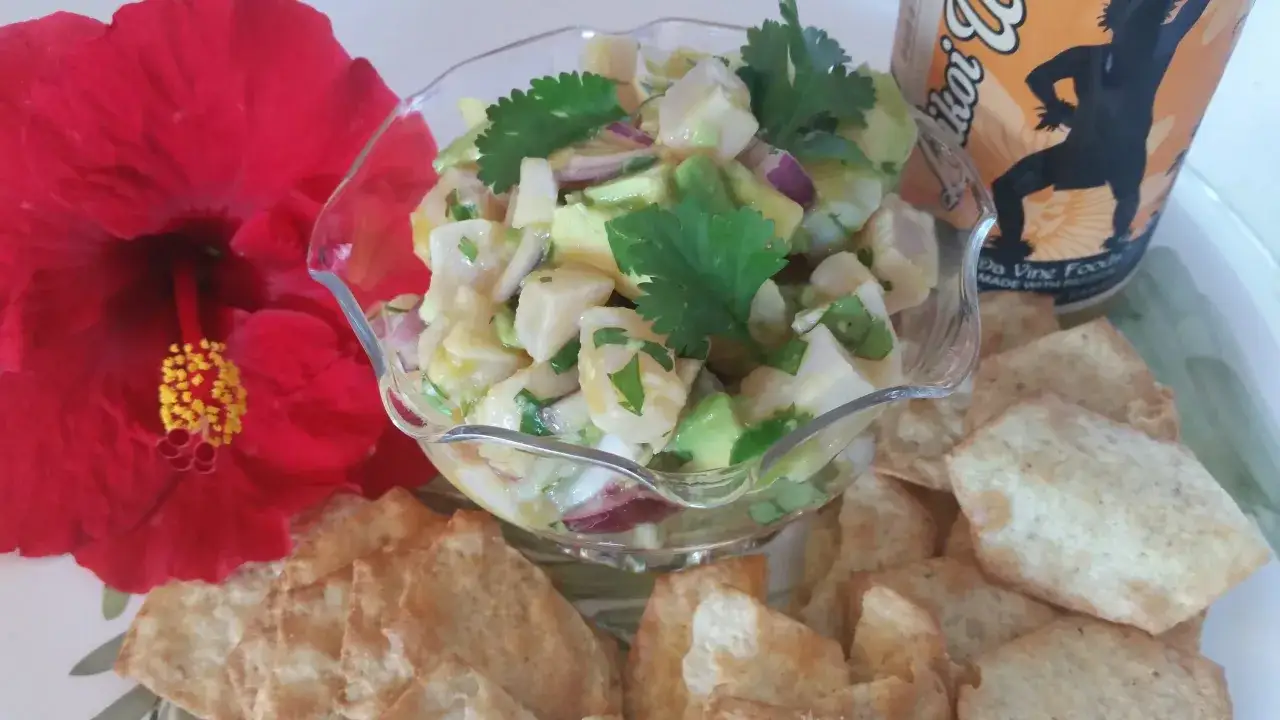 Frischer Fisch-Ceviche-Salat mit Avocado, Koriander und roten Zwiebeln, serviert mit Tortilla-Chips. Eine rote Hibiskusbl&uuml;te und eine Dose Getr&auml;nk mit der Aufschrift 