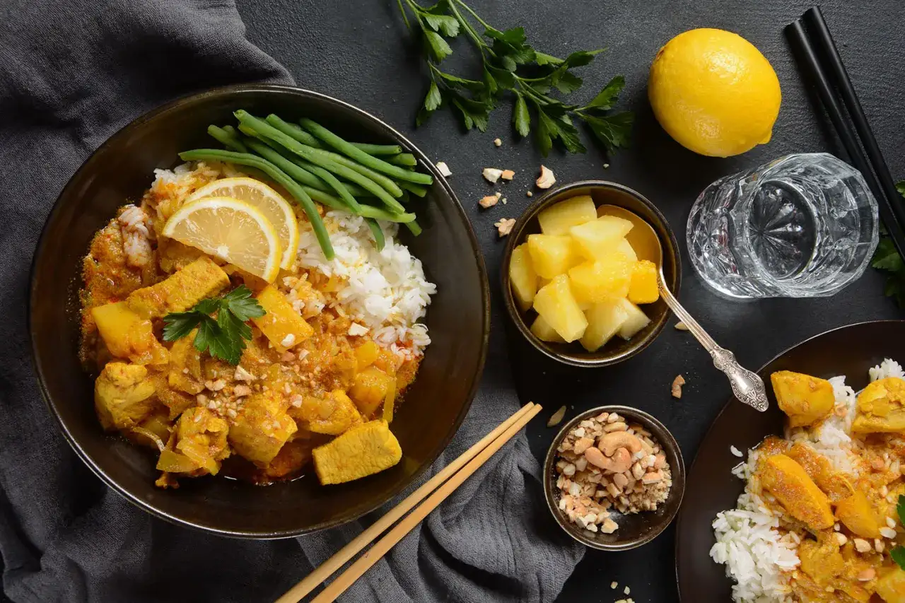 Ein k&ouml;stliches Massaman Curry Rezept mit H&uuml;hnchen, Reis, gr&uuml;nen Bohnen und Ananas. Dazu Cashewkerne und eine Zitronenspalte.