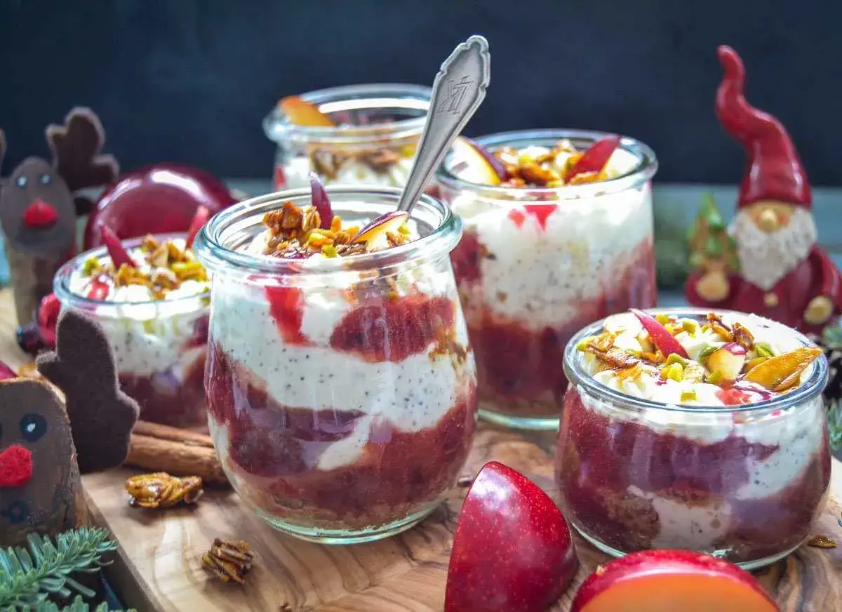 Ausgefallenes weihnachtsdessert im Glas: Schichten aus cremiger Mousse, roter Fruchtso&szlig;e und knusprigem Topping, garniert mit Apfelst&uuml;cken und Pistazien. Perfekt f&uuml;r die Feiertage!