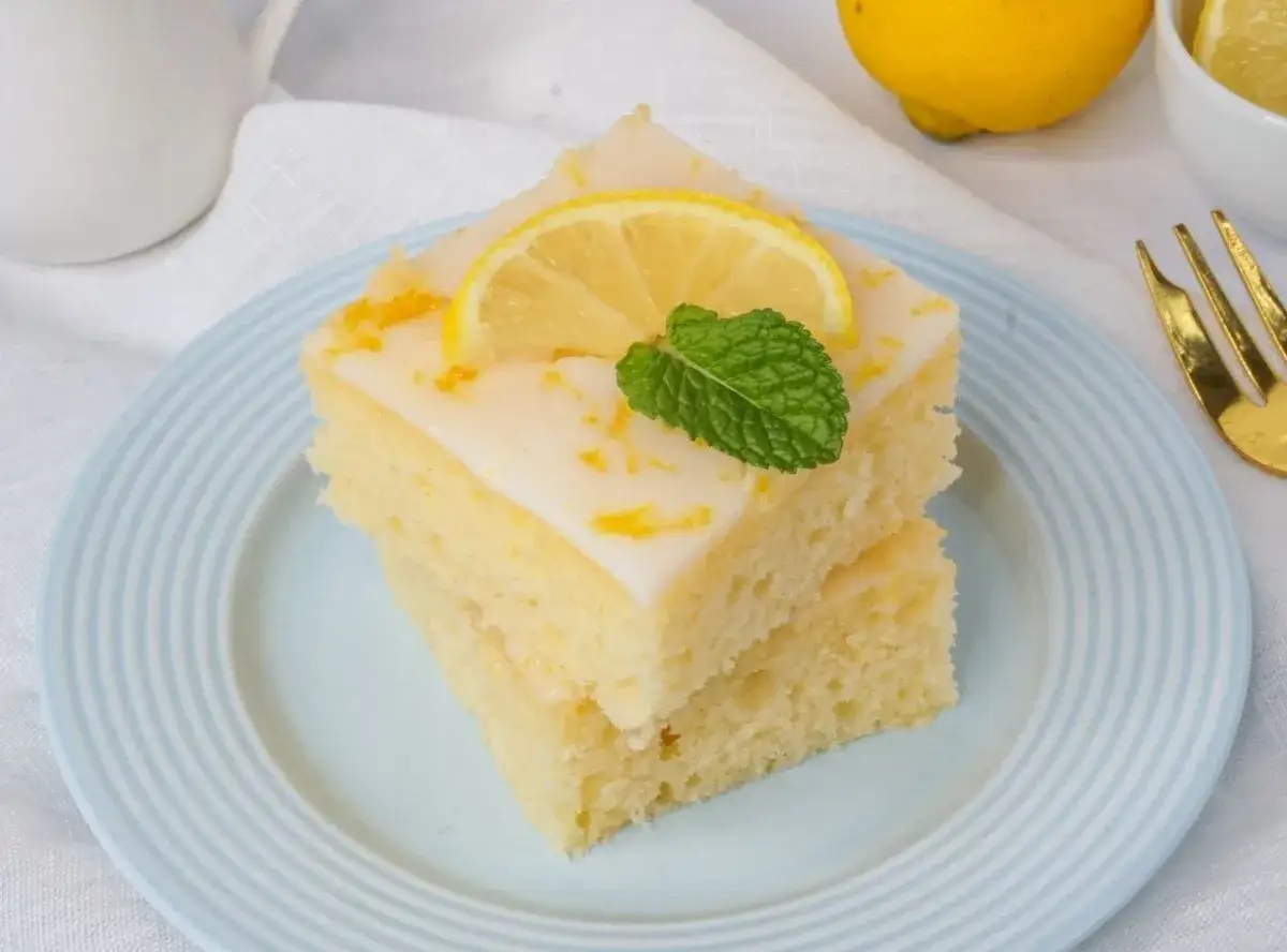 Zwei Stücke weltbester saftiger zitronenkuchen mit joghurt, garniert mit Zitronenscheibe und Minze.
