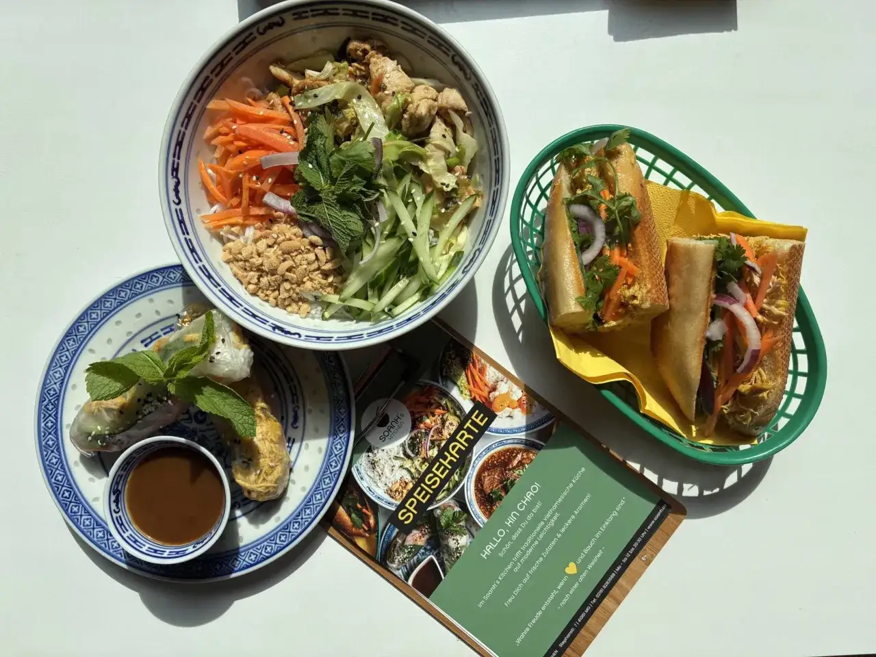 Vietnamesische Rezepte: Bunte Sch&uuml;ssel mit H&auml;hnchen, Reisnudeln, Gem&uuml;se und Erdn&uuml;ssen, dazu Banh Mi und Sommerrollen.