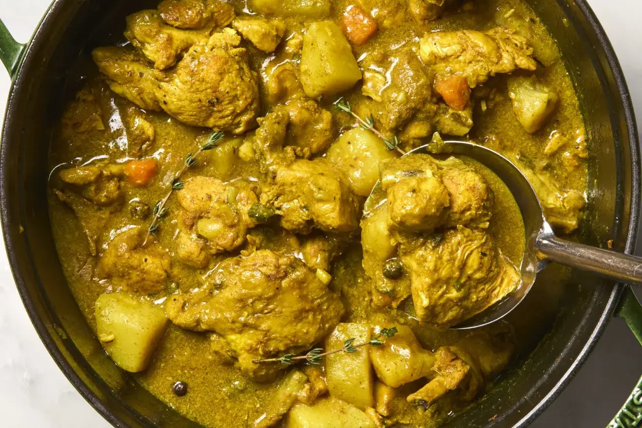 Ein köstlicher Colombo de Poulet in einem Topf, mit zarten Hühnerstücken, Kartoffeln und Karotten in einer würzigen gelben Sauce.