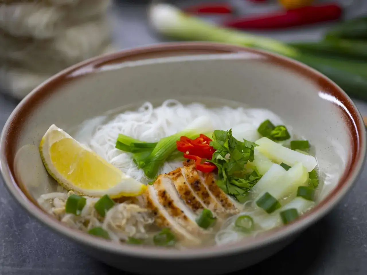 Eine Sch&uuml;ssel mit bun rieu: Reisnudeln, gegrilltes H&auml;hnchen, Zitrone, Fr&uuml;hlingszwiebeln, Chili und Kr&auml;utern in Br&uuml;he.