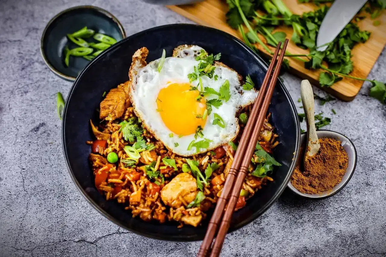 Ein k&ouml;stliches Nasi Goreng Rezept Original mit gebratenem Ei, H&uuml;hnchen, Erbsen und Koriander. Dazu ein L&ouml;ffel Gew&uuml;rzmischung.