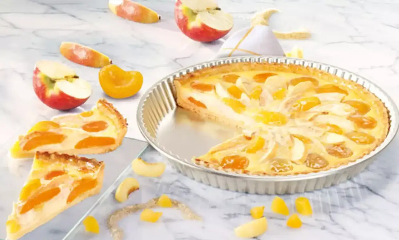 Eine köstliche Tarte aux fruits mit Apfel- und Aprikosenstücken, umgeben von frischen Früchten und zwei angeschnittenen Tortenstücken.