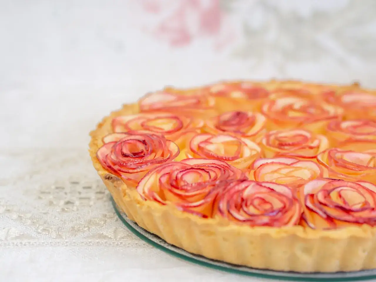 Ein k&ouml;stlicher Apfelrosen Kuchen, kunstvoll mit Apfelscheiben zu Rosen geformt, auf einem zarten Spitzentuch.