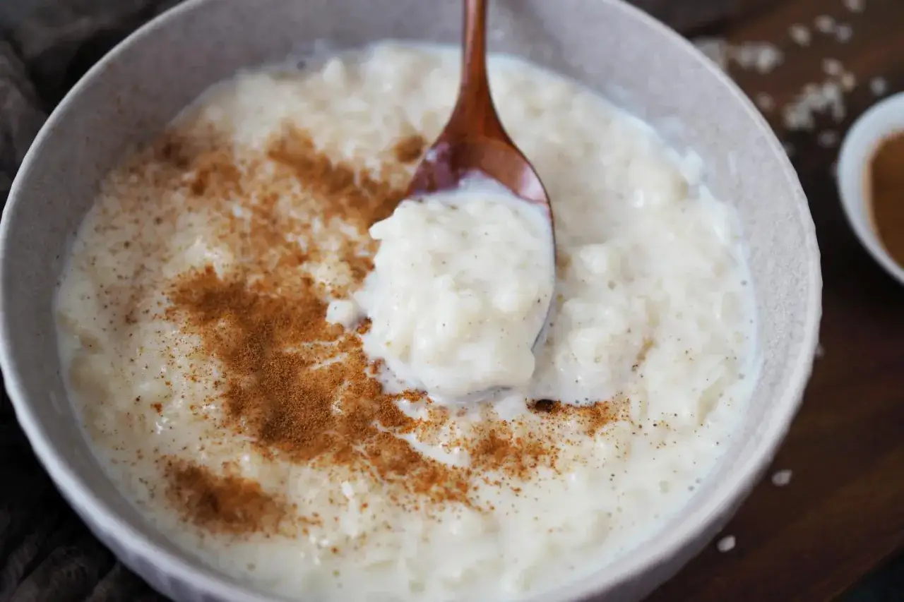 Cremiger Milchreis mit Wasser gekocht, bestreut mit Zimt. Eine L&ouml;ffelprobe zeigt die weiche Konsistenz.