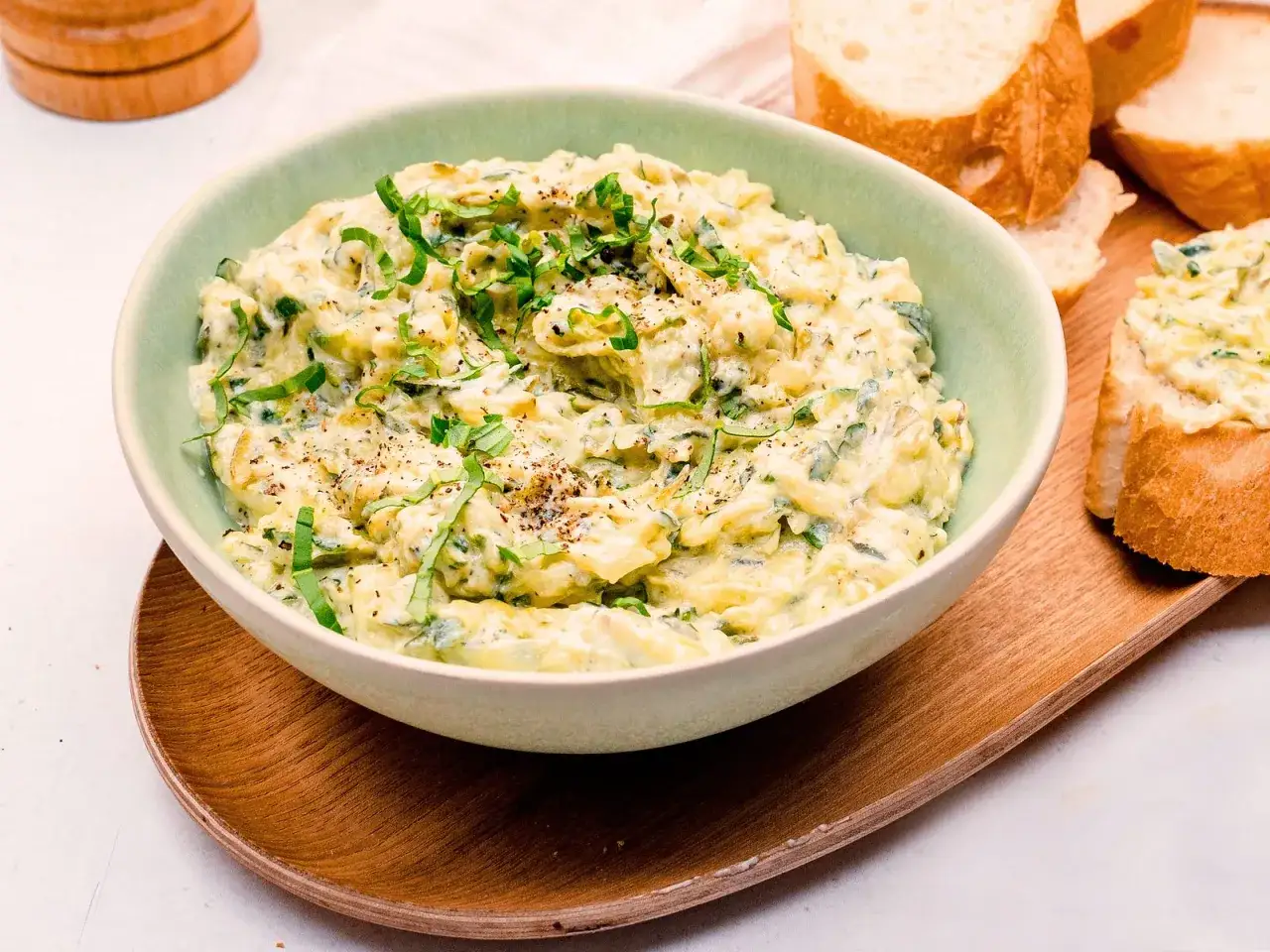Cremiger Zucchini-Aufstrich mit Kr&auml;utern, garniert mit Pfeffer, serviert in einer Sch&uuml;ssel mit Baguettescheiben.