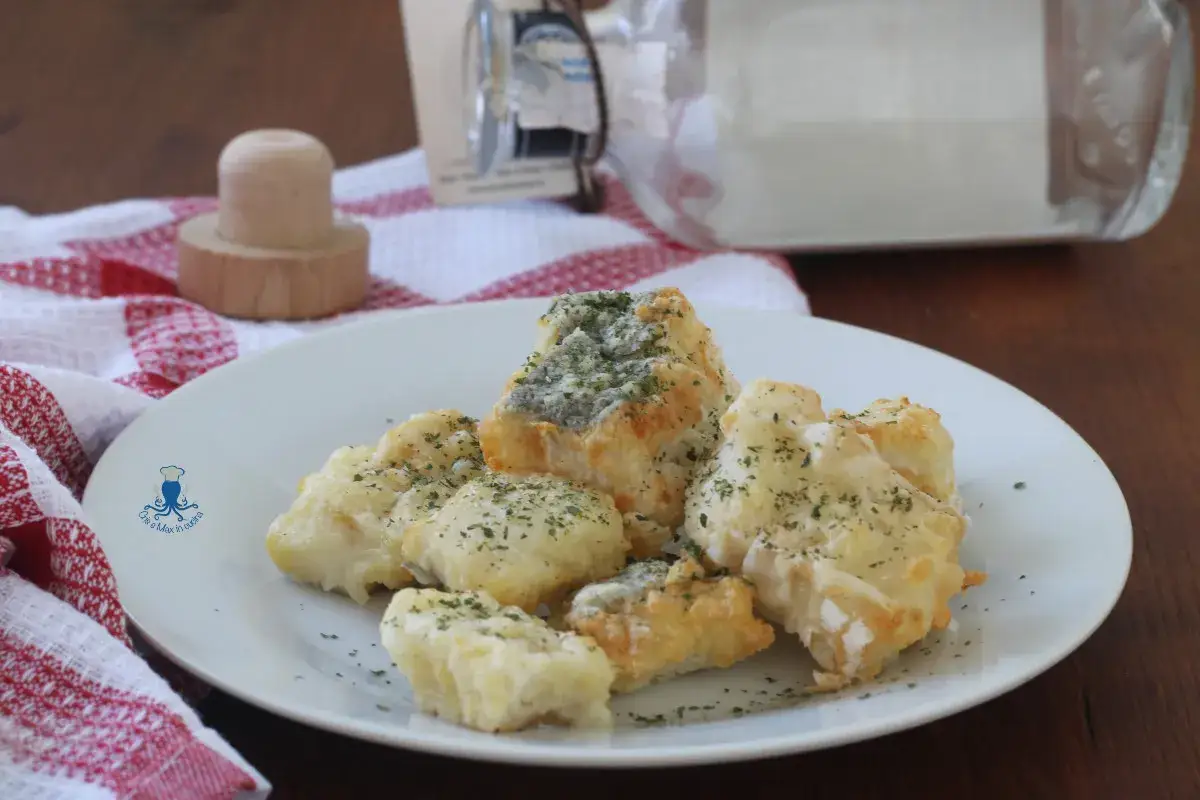 Knusprige Accras de Morue, kleine frittierte Fischb&auml;llchen, bestreut mit Kr&auml;utern, auf einem wei&szlig;en Teller serviert.