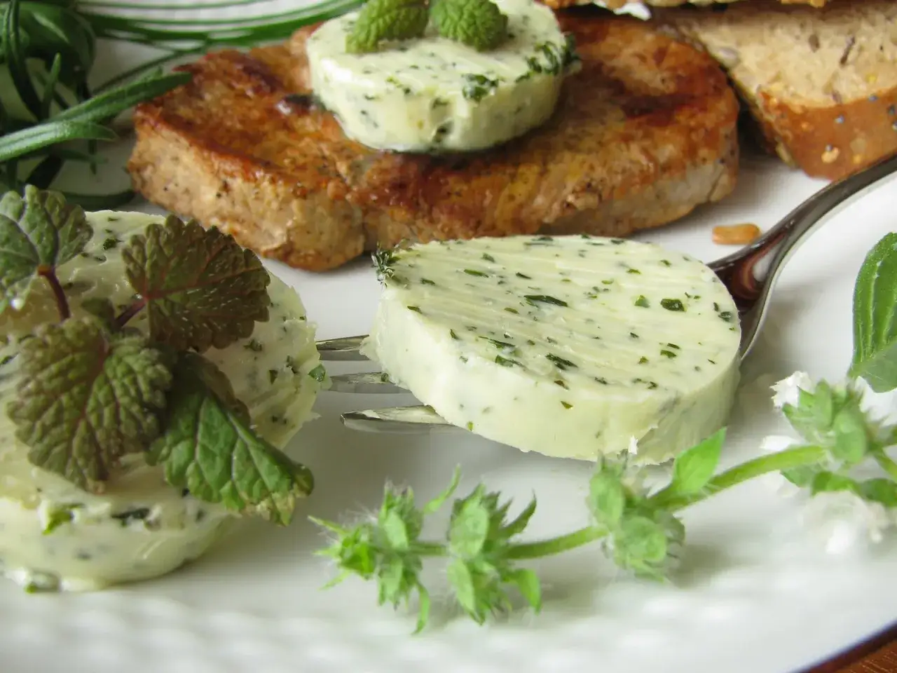 Kr&auml;uterbutter-Scheiben auf einem Teller mit Steak und Brot. K&ouml;stliche Butter Rezepte f&uuml;r jeden Anlass.