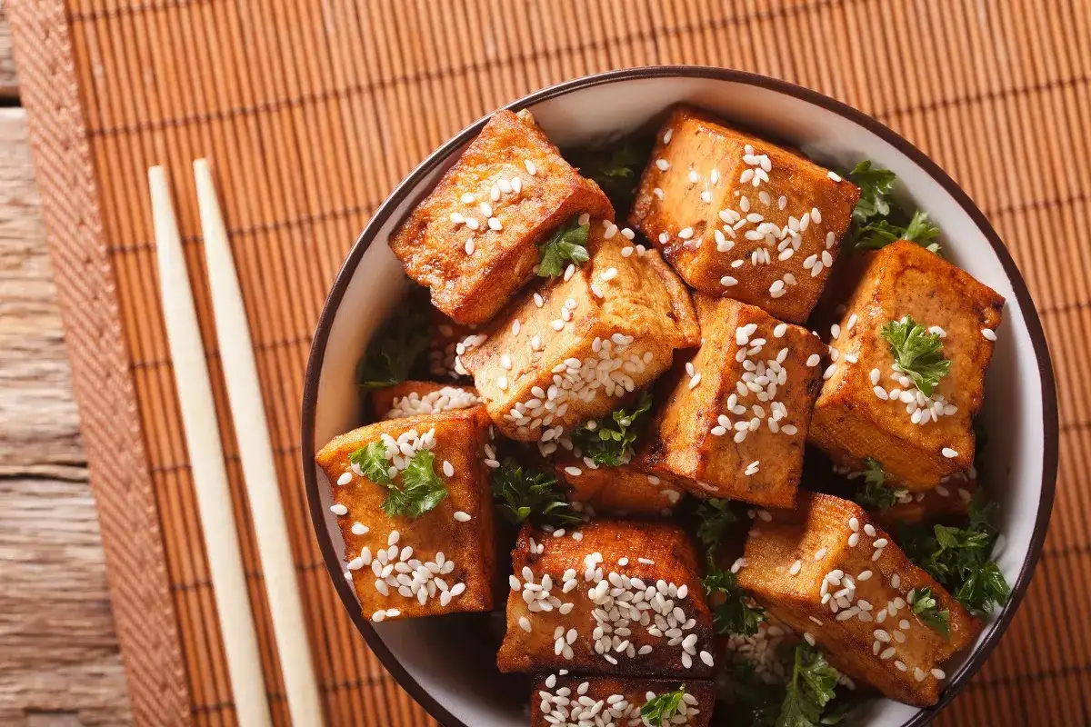 Knusprig gebratene Tofuw&uuml;rfel, bestreut mit Sesam und Petersilie, serviert in einer Sch&uuml;ssel. Dieses tofu fleisch ist eine k&ouml;stliche vegetarische Option.