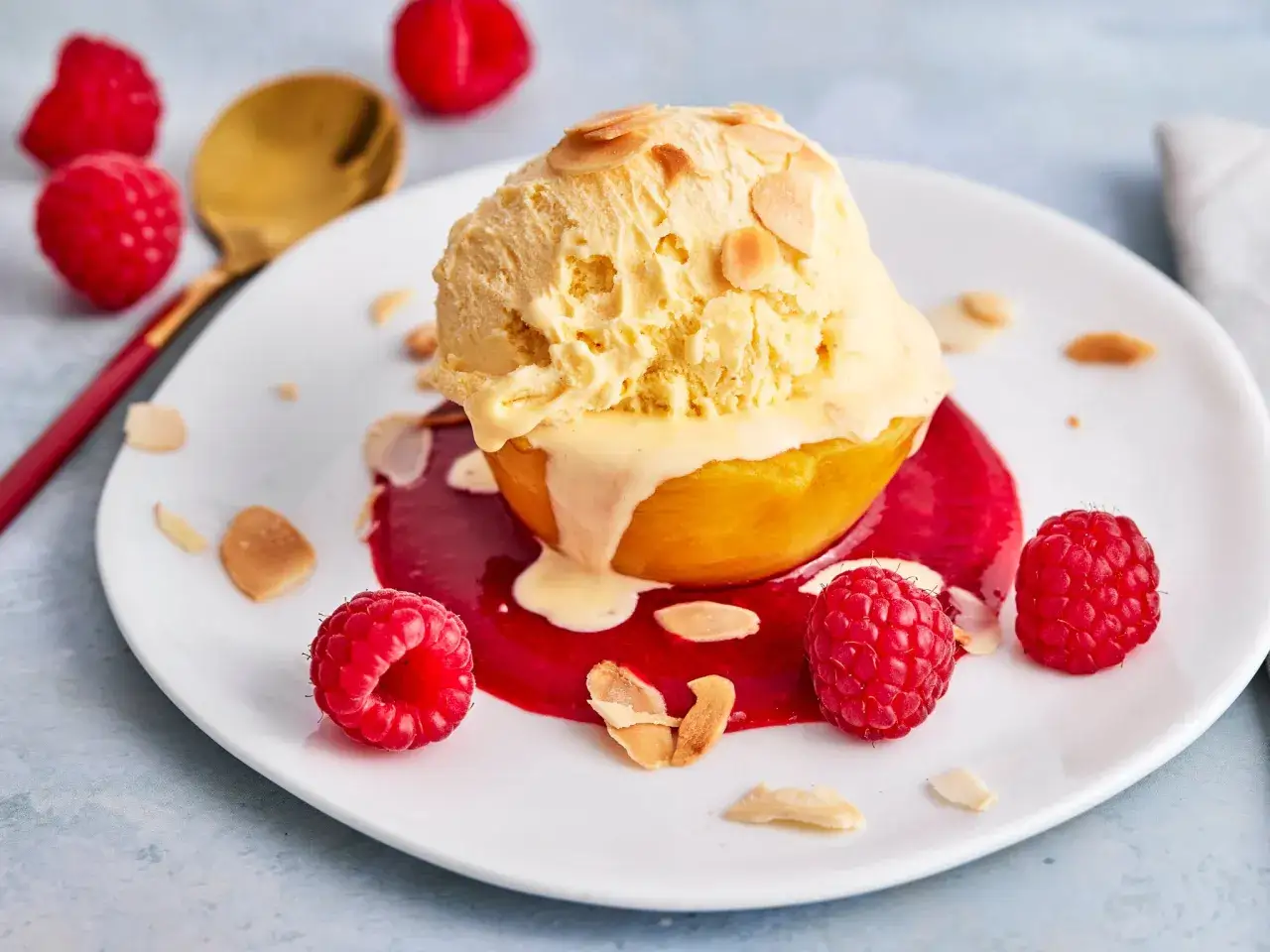 Ein Pfirsich Melba Dessert mit einer Kugel Vanilleeis, Himbeersauce und frischen Himbeeren, garniert mit Mandelbl&auml;ttchen.